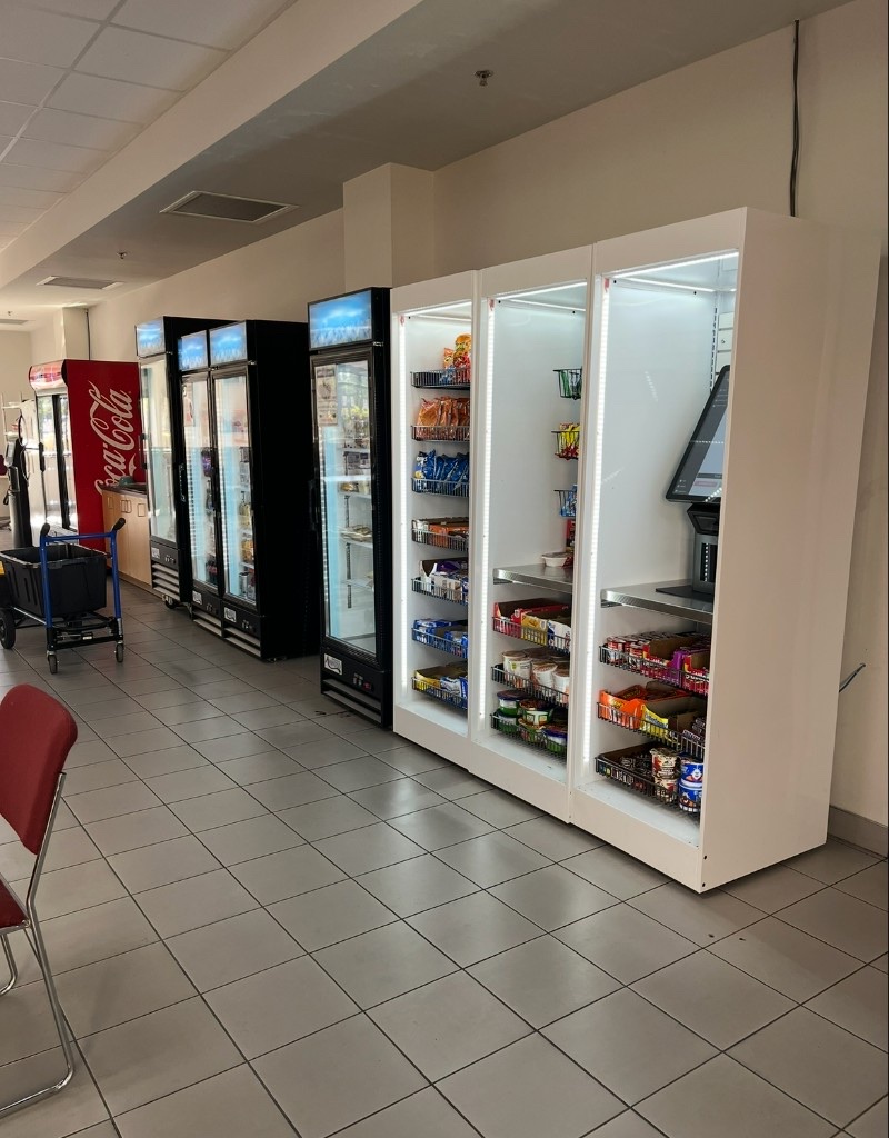 A stocked workplace refreshment area with snacks, refrigerated drinks, and vending equipment